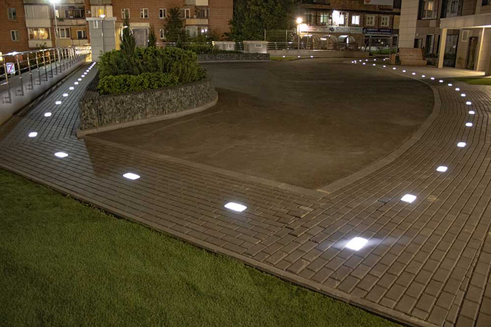 На фотографии тротуарная плитка производства "Ulkon" светится во дворе жилого дома